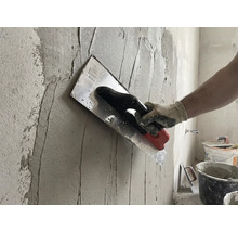 Un artisan applique du plâtre sur un mur avec une taloche.