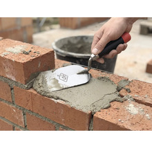 Maçonnerie : une brique est jointoyée avec du mortier et une truelle.