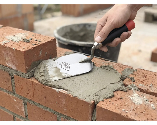 Maçonnerie : une brique est jointoyée avec du mortier et une truelle.