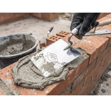 Maçon au travail avec truelle, mortier et briques