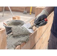 Maçon appliquant du mortier et des briques pour la construction d'un mur