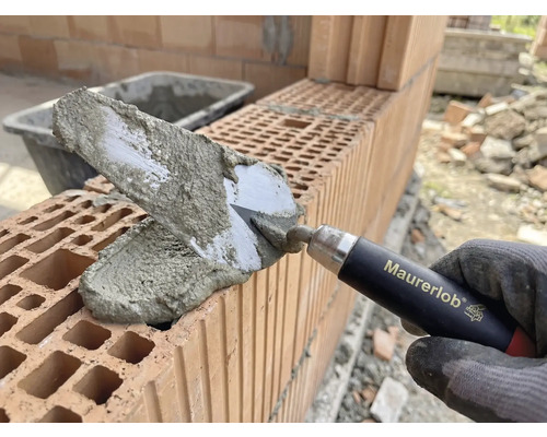 Main de maçon avec truelle appliquant du mortier sur des briques