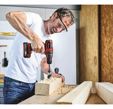 Mann bohrt mit einem Akku-Bohrschrauber ein Loch in ein Holzstück