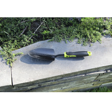 Petite pelle de jardin sur un mur avec des plantes en arrière-plan