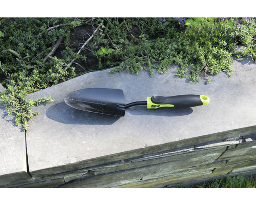 Petite pelle de jardin sur un mur avec des plantes en arrière-plan