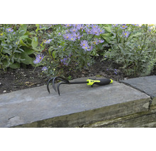 Griffe de jardin à trois dents et manche en plastique devant un parterre de fleurs