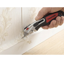 Main avec un cutter Rautner coupant avec précision du papier peint à motif floral le long d une plinthe.