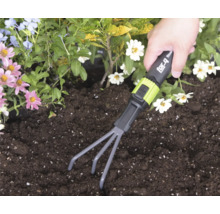 Une main utilise un petit râteau for_q dans de la terre au milieu de fleurs colorées.