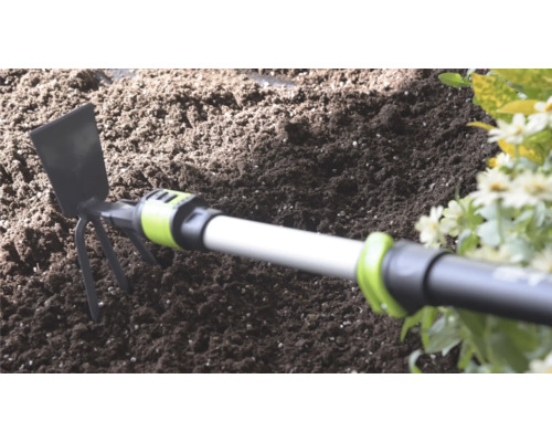 Serfouette avec lame en métal et trois dents dans du terreau sombre à côté de fleurs.