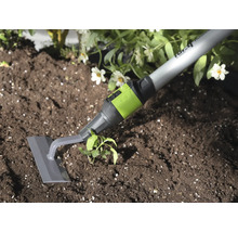 Sarcloir de jardin avec lame grise et raccord vert utilisé pour désherber la terre à côté d'une plante.