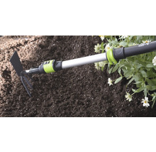 Serfouette for_q avec manche télescopique utilisée dans la terre à côté de fleurs lors de travaux de jardinage.