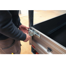 Person bedient einen Winkelhebelverschluss an einer silbernen Pkw-Anhänger-Bordwand aus Metall.