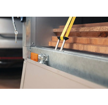 Gelber Spanngurt fixiert Holzbretter auf einem Anhänger zur Ladungssicherung mit Doppelhaken aus Metall.