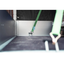 Grüner Spanngurt mit Haken in einer Verzurröse auf der Ladefläche eines Anhängers zur Ladungssicherung.