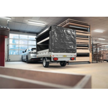 Einachsiger Humbaur PKW-Anhänger mit grauer Hochplane in einer Lagerhalle neben Holzregalen und einem Auto.