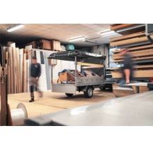 Humbaur Anhänger mit schwarzer Hochplane in einer hellen, gut organisierten Werkstatt mit Holzplatten und Baumaterialien.