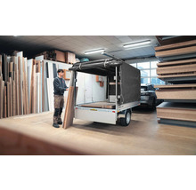 Eine Person belädt einen Anhänger mit Hochplane in einem Lager mit Holzplatten.