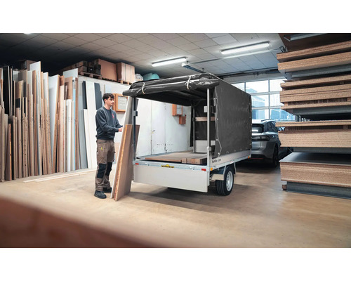 Eine Person belädt einen Anhänger mit Hochplane in einem Lager mit Holzplatten.