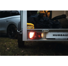 Feu arrière allumé et support de plaque d'immatriculation sur une remorque Humbaur, chargée de sacs et de sangles.