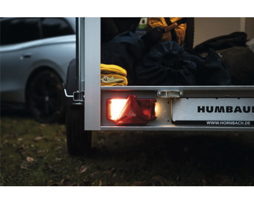 Feu arrière allumé et support de plaque d'immatriculation sur une remorque Humbaur, chargée de sacs et de sangles.