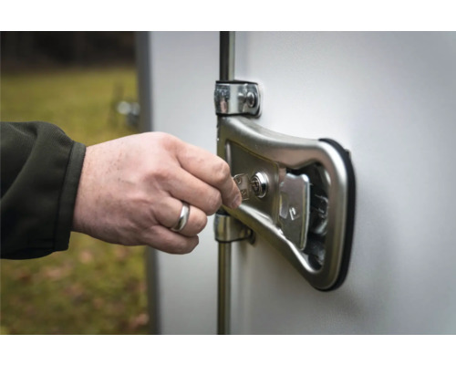 Une main insère une clé métallique dans la serrure du verrou de porte d'une remorque.
