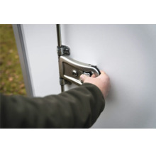 Main actionnant un verrou à levier en métal avec cylindre sur une porte blanche.