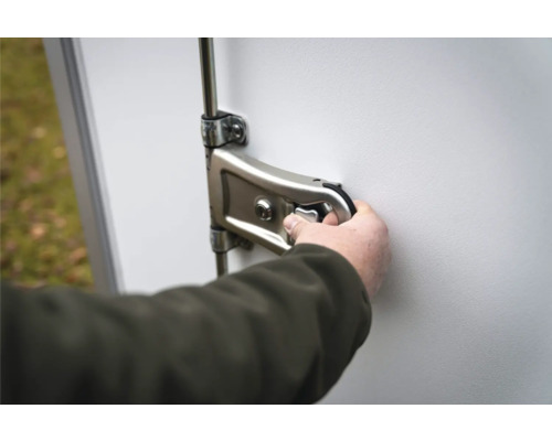 Main actionnant un verrou à levier en métal avec cylindre sur une porte blanche.