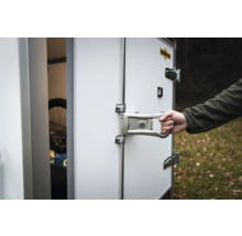 Main actionnant le verrou de porte métallique d'une remorque fourgon Humbaur blanche avec Humbaur Logo.