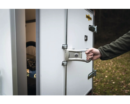 Main actionnant le verrou de porte métallique d'une remorque fourgon Humbaur blanche avec Humbaur Logo.