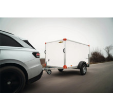 Une voiture argentée tracte une remorque fourgon Humbaur blanche sur une route.
