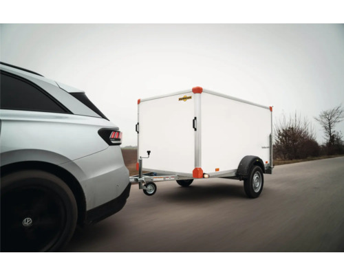 Une voiture argentée tracte une remorque fourgon Humbaur blanche sur une route.