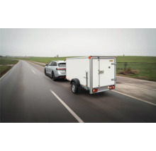 Remorque fourgon Humbaur à un essieu blanche tractée par un SUV argenté sur une route mouillée.