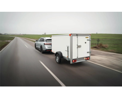 Remorque fourgon Humbaur à un essieu blanche tractée par un SUV argenté sur une route mouillée.