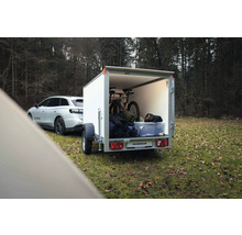 Remorque fourgon Humbaur blanche attelée à une voiture, chargée d'un VTT et de matériel dans une forêt.