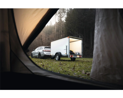 Voiture argentée avec une remorque fourgon blanche dans un champ devant une forêt, vue depuis l'intérieur d'une tente.