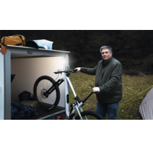 Un homme se tient à l extérieur à côté d une remorque fermée éclairée et tient un vélo tout terrain blanc.