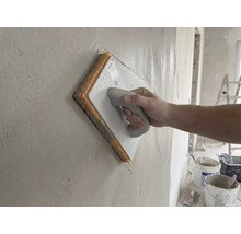 Main utilisant une taloche avec éponge sur un mur fraîchement enduit.
