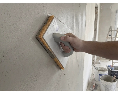 Main utilisant une taloche avec éponge sur un mur fraîchement enduit.