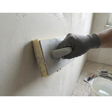 Main gantée utilisant une taloche éponge pour lisser de l'enduit sur un mur.
