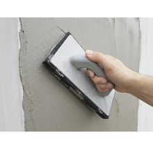 Une main lisse l'enduit frais sur un mur avec une taloche éponge.