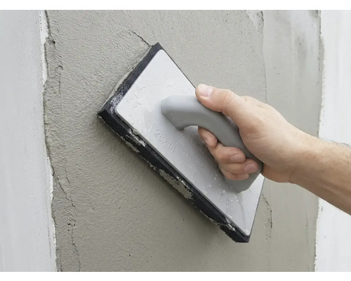 Une main lisse l'enduit frais sur un mur avec une taloche éponge.