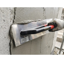 Utilisation d une lisseuse Maurerlob pour enduire un mur en béton avec du mortier par une personne portant un gant de travail.