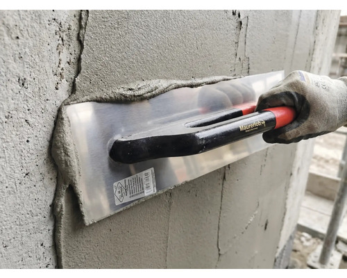 Utilisation d une lisseuse Maurerlob pour enduire un mur en béton avec du mortier par une personne portant un gant de travail.