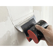 Une main applique de l'enduit sur un mur avec un couteau à enduire large.