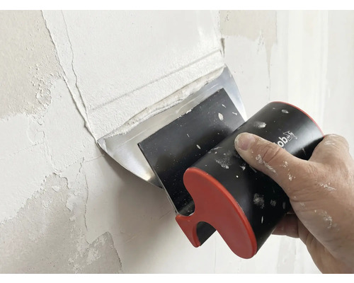 Une main applique de l'enduit sur un mur avec un couteau à enduire large.