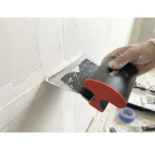 Main utilisant un couteau à enduire large pour appliquer et lisser de l'enduit blanc sur un joint de mur.