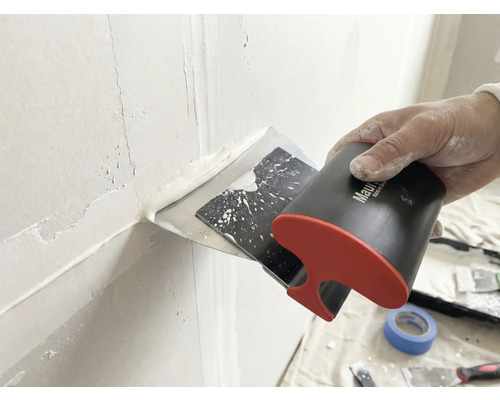 Main utilisant un couteau à enduire large pour appliquer et lisser de l'enduit blanc sur un joint de mur.