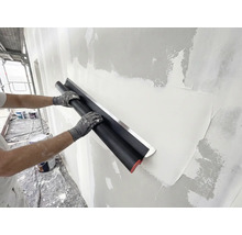 Person glättet Putz an einer Wand mit einem breiten Flächenspachtel aus Edelstahl während Renovierungsarbeiten.