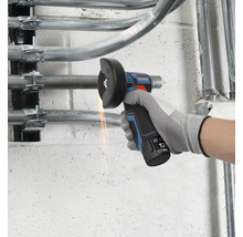 Bosch Professional 12 Volt Akku-Winkelschleifer trennt ein Metallrohr an einer Wand mit sichtbarem Funkenflug.
