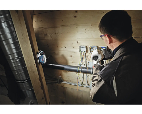 Ein Bosch Akku-Baustrahler beleuchtet einen Handwerker bei Elektroarbeiten an einer Holzwand.